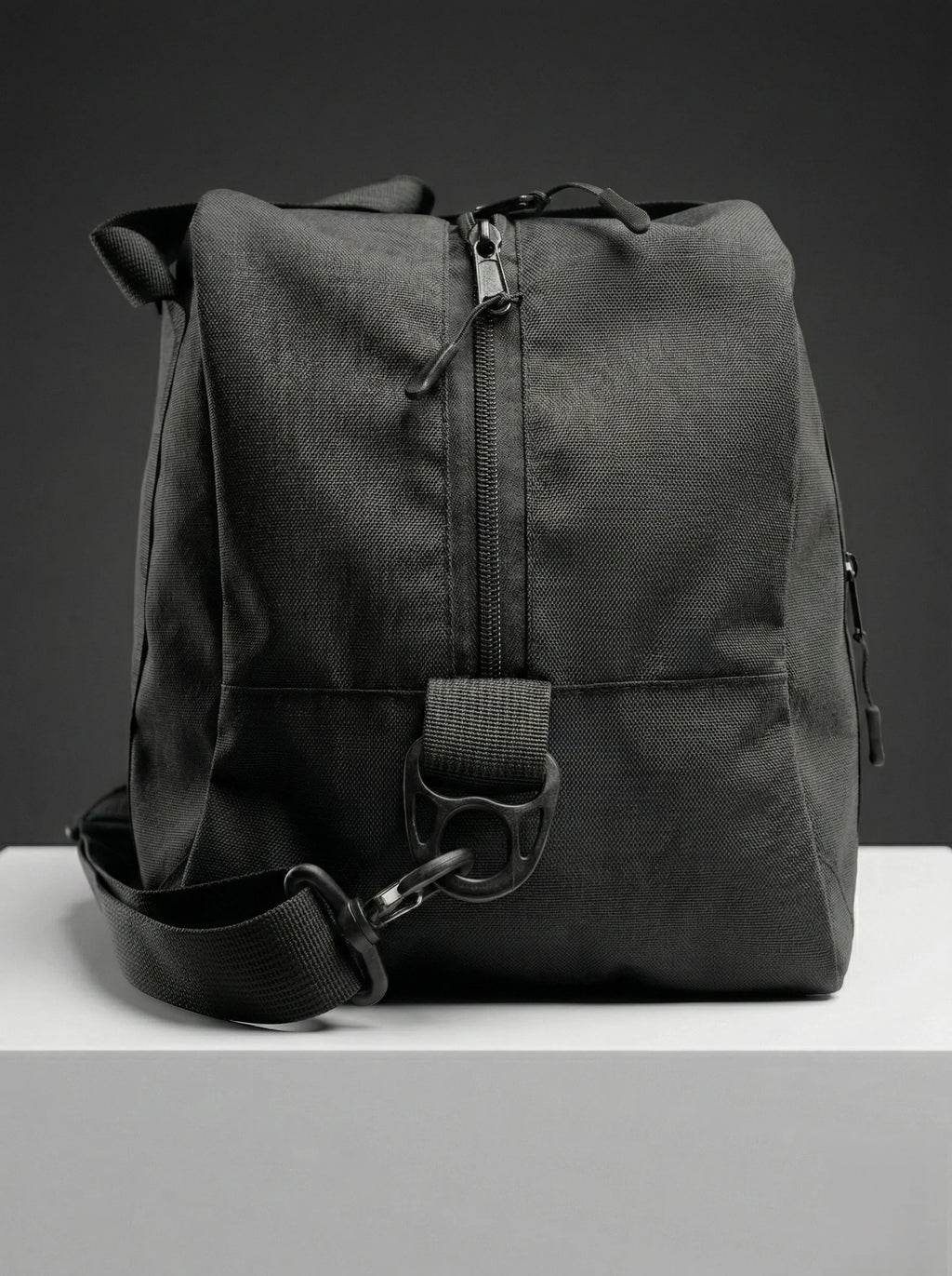 Black EQ1 duffel bag with sturdy handles, adjustable shoulder strap, and spacious travel-friendly design placed on a white platform.