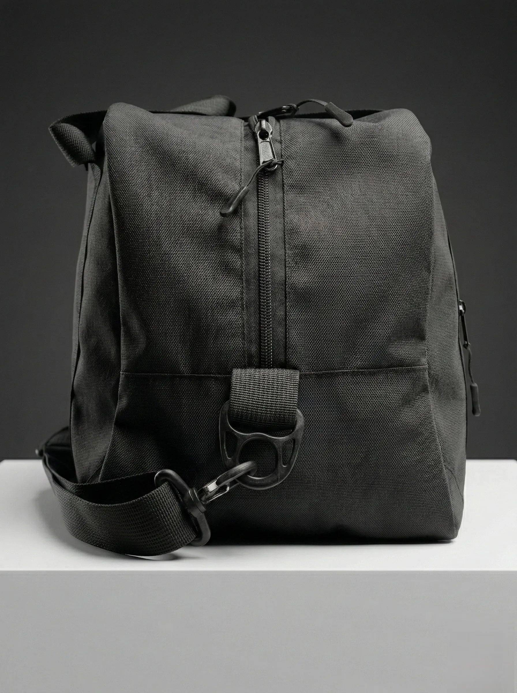 Black EQ1 duffel bag with sturdy handles, adjustable shoulder strap, and spacious travel-friendly design placed on a white platform.