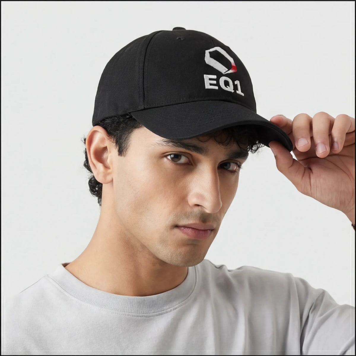 Person adjusting a black EQ1 cap while wearing a light gray shirt