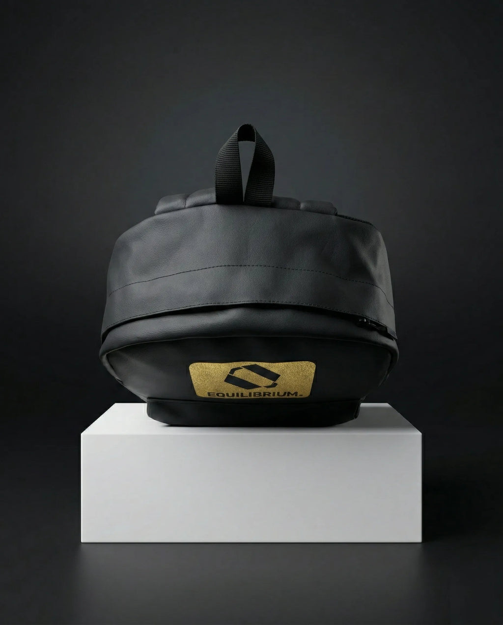 Black EQ1 premium backpack placed on a white display box with a dark background and gold Equilibrium logo branding.