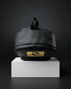 Black EQ1 premium backpack placed on a white display box with a dark background and gold Equilibrium logo branding.