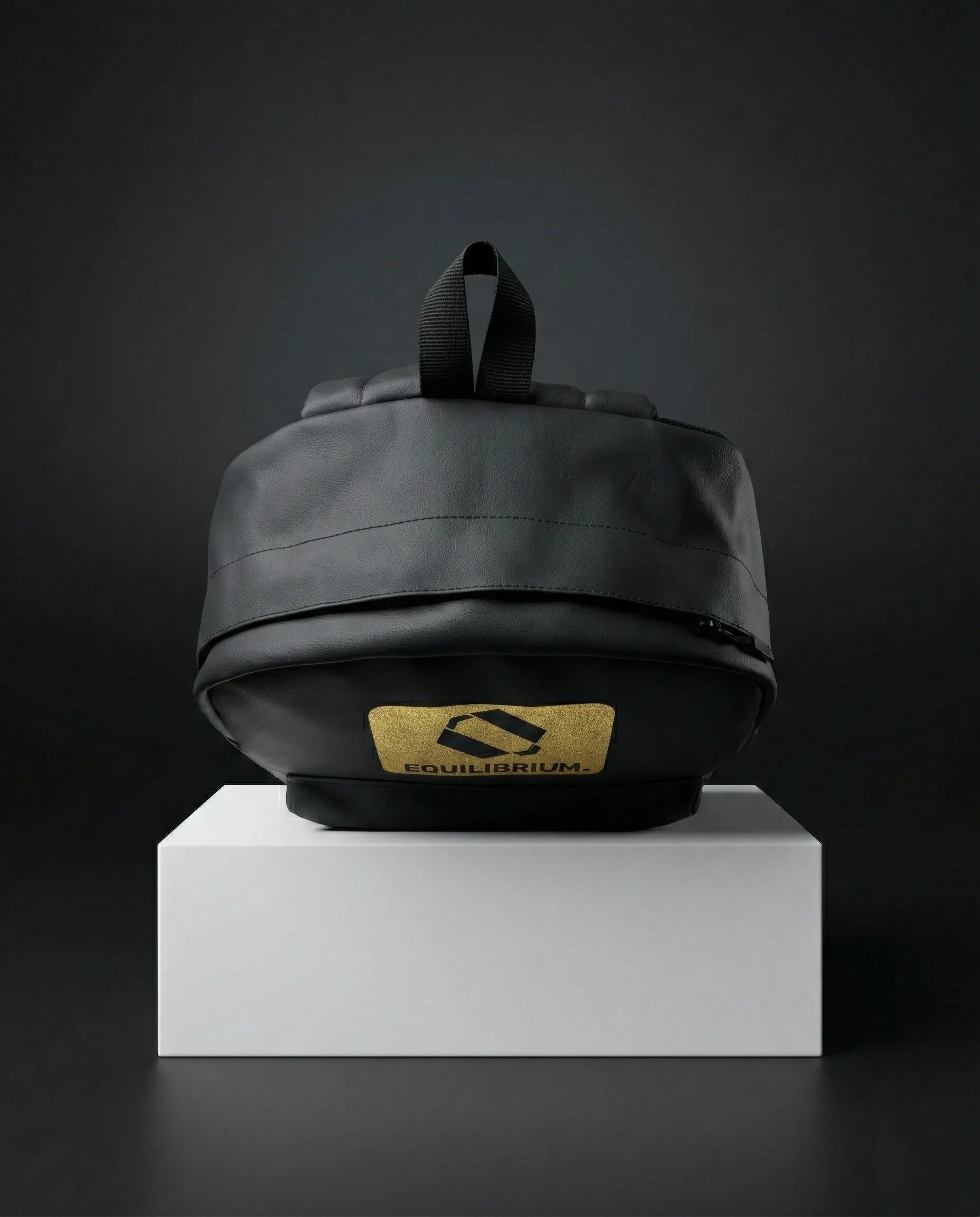 Black EQ1 premium backpack placed on a white display box with a dark background and gold Equilibrium logo branding.