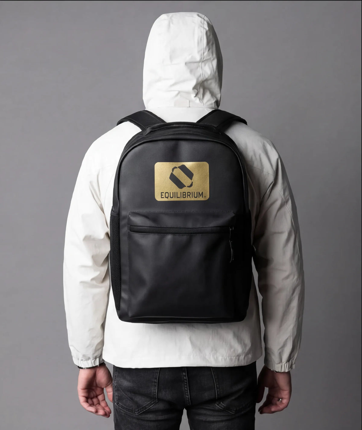Person wearing black Equilibrium backpack with front pocket and gold logo design