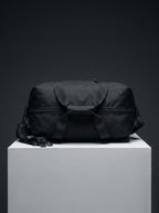 Top view of black EQ1 duffel bag featuring strong handles, zipper closure, and durable travel-ready structure on a white display platform.